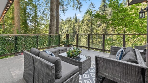 An outdoor patio with wicker furniture, a patterned floor, and a view of a forest. - Capilano Forest Retreat | 3BD/2BA Suite (North Vancouver)
