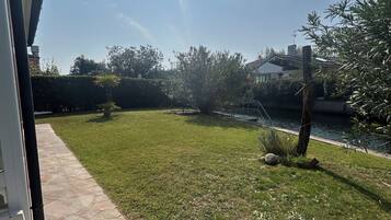 A grassy outdoor area with a stone pathway, a small tree, and a body of water.