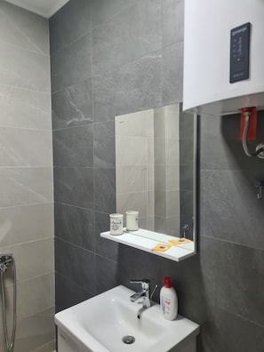 Une salle de bain avec un lavabo blanc, un miroir, une étagÚre contenant des articles de toilette et un espace douche.