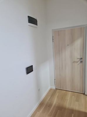 Une piÚce avec une porte en bois, un mur blanc et un thermostat fixé au mur.