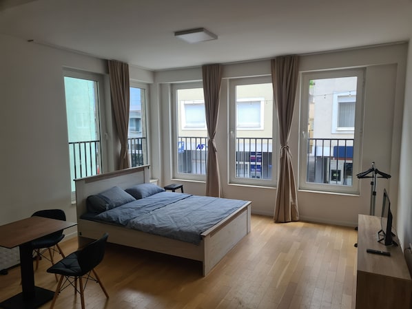 Une chambre Ă coucher avec un lit, un bureau et deux fenĂȘtres avec des rideaux.