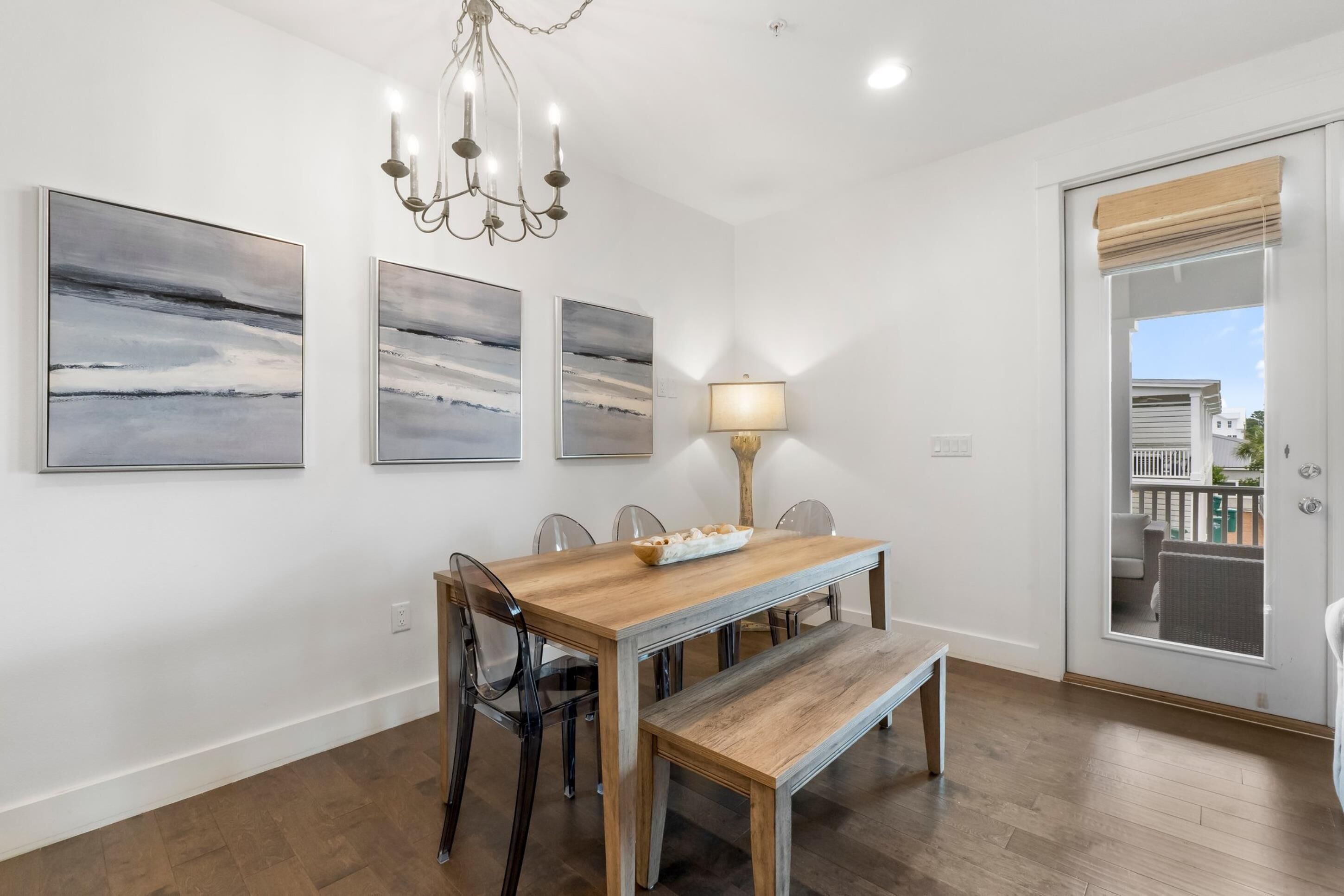 A dining area with a wooden table, chairs, a bench, and three wall-mounted paintings.