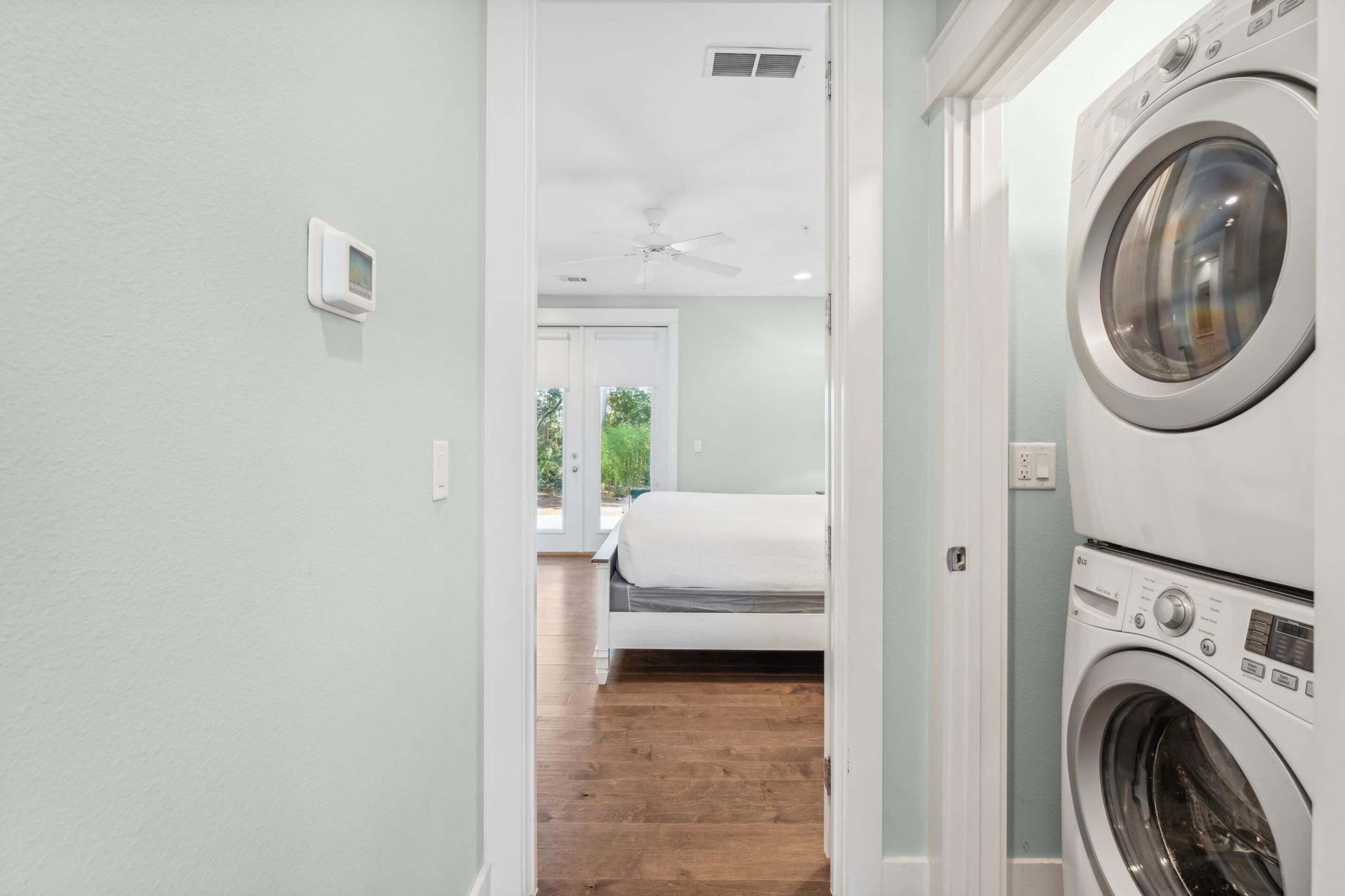 A laundry room with a washing machine and dryer, a bed in the adjacent room, and a ceiling fan.