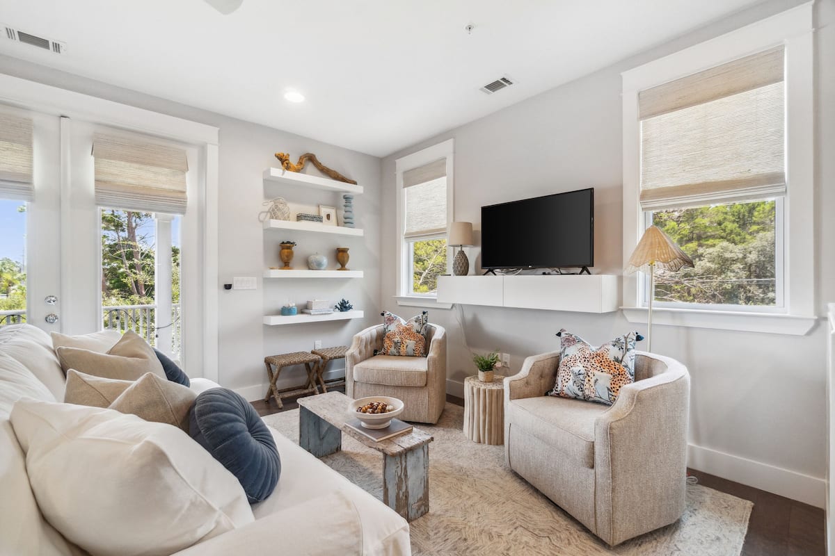 A modern living room with a sofa, armchairs, a coffee table, and a TV mounted on the wall.