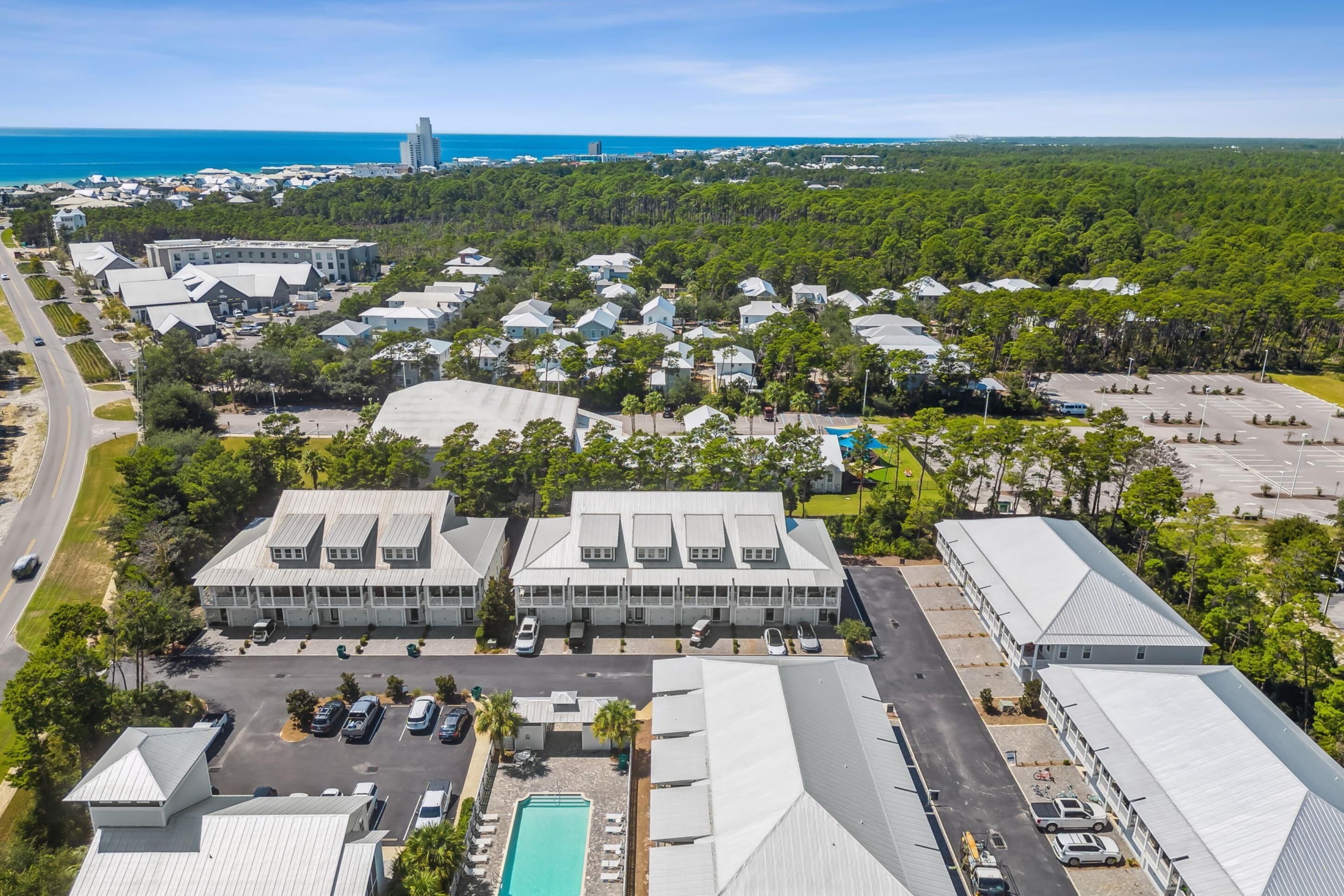 An aerial view of a resort with multiple buildings, a parking lot, and a view of the ocean.