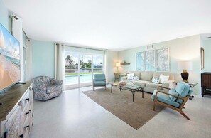 Ein geräumiges Wohnzimmer mit großem Fenster, einer Couch, einem Couchtisch und einem Fernseher.