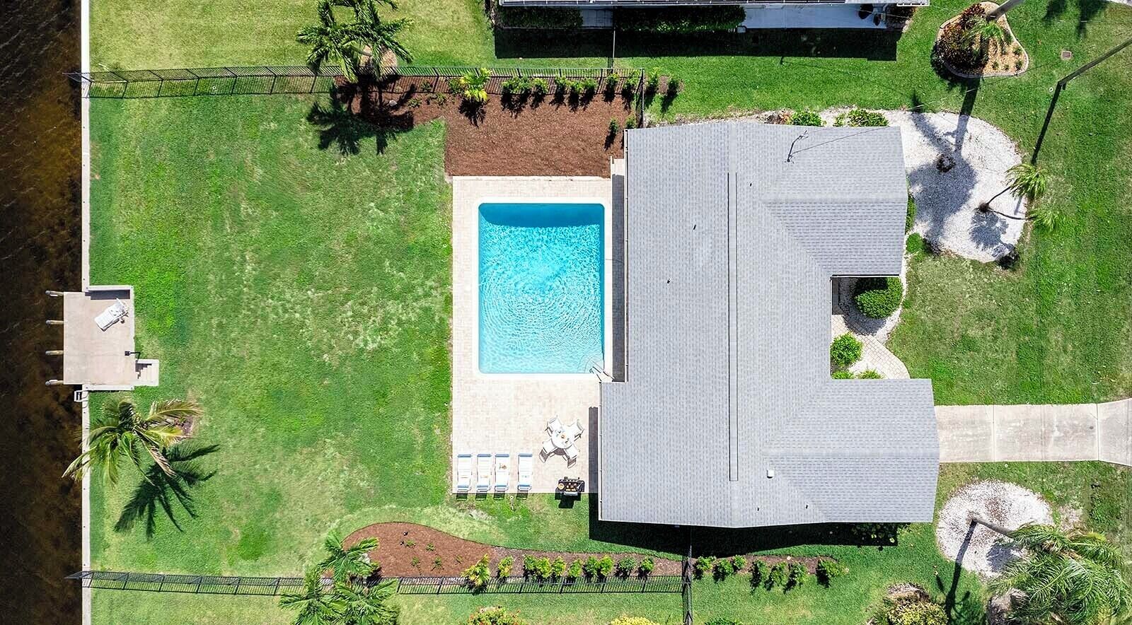 An aerial view of a property with a swimming pool, a covered patio, and a landscaped lawn.