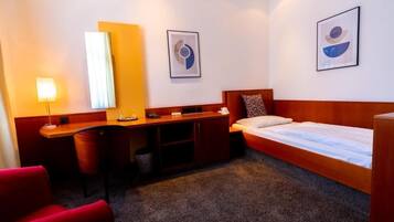Habitación de hotel con cama, escritorio, silla, lámpara y dos obras de arte abstractas en la pared.