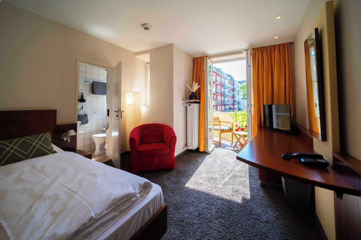 Habitación de hotel con cama, escritorio, silla, televisión y vista al exterior.