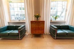 Una habitación con dos sofás verdes, un aparador de madera con cajones y una ventana con cortinas.
