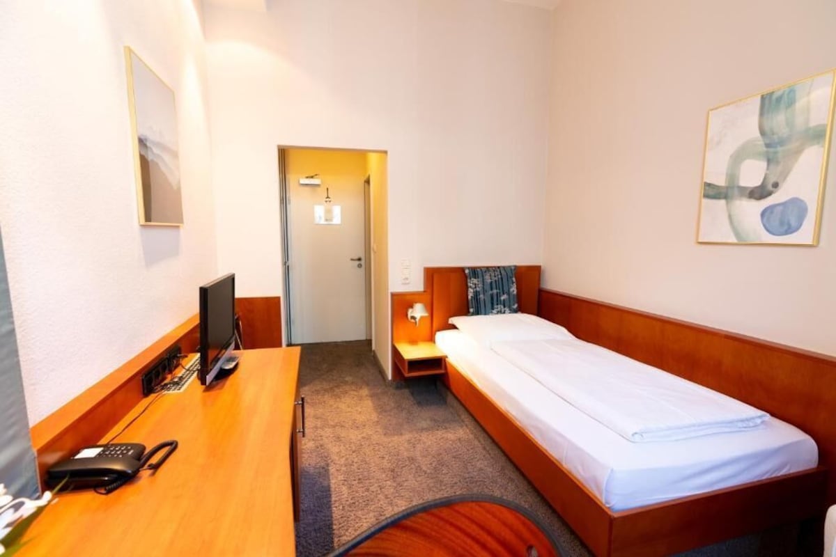 Una habitación de hotel con un escritorio de madera, una cama, un televisor y una puerta que da a un baño.