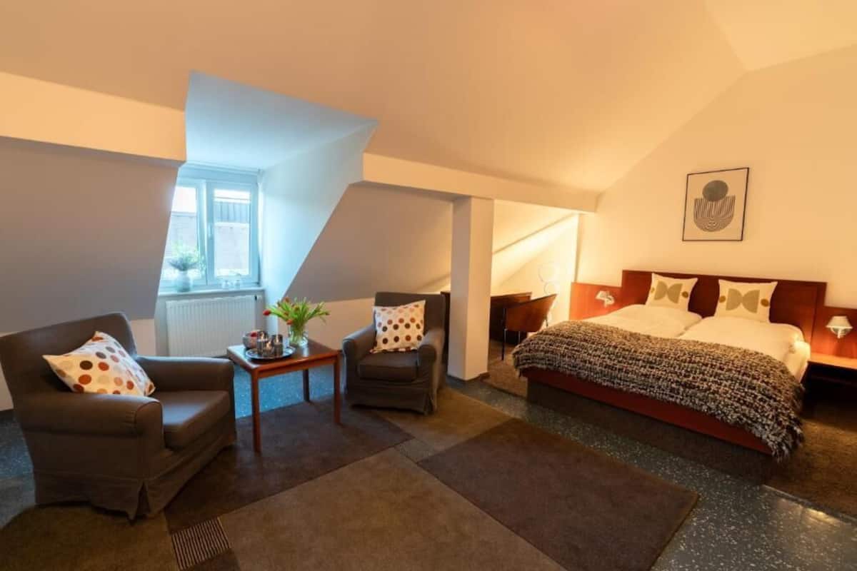 Una moderna camera d'albergo con un letto, due poltrone, un tavolino e una finestra.