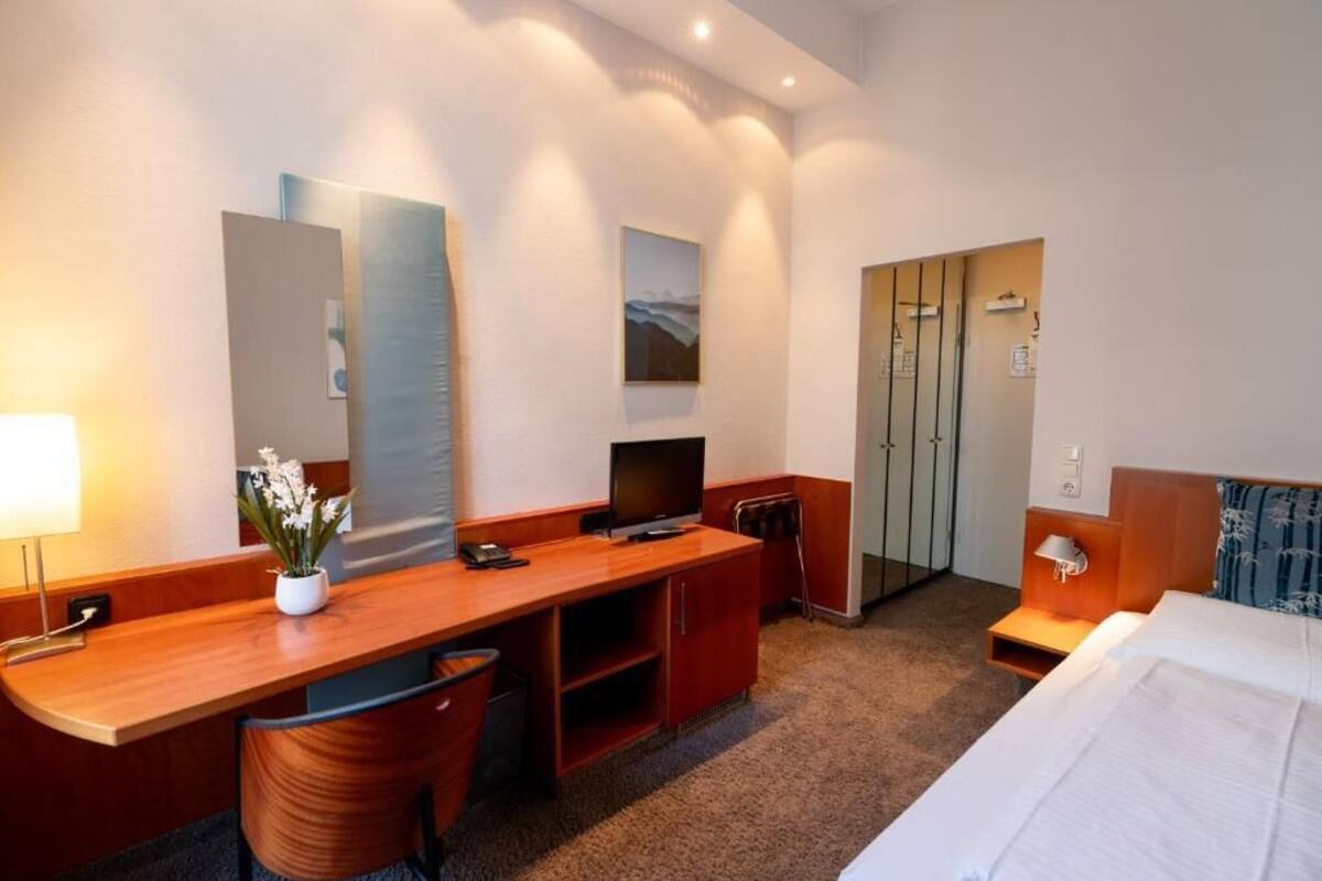 Una camera d'albergo con una scrivania in legno, una televisione, un letto e uno specchio.