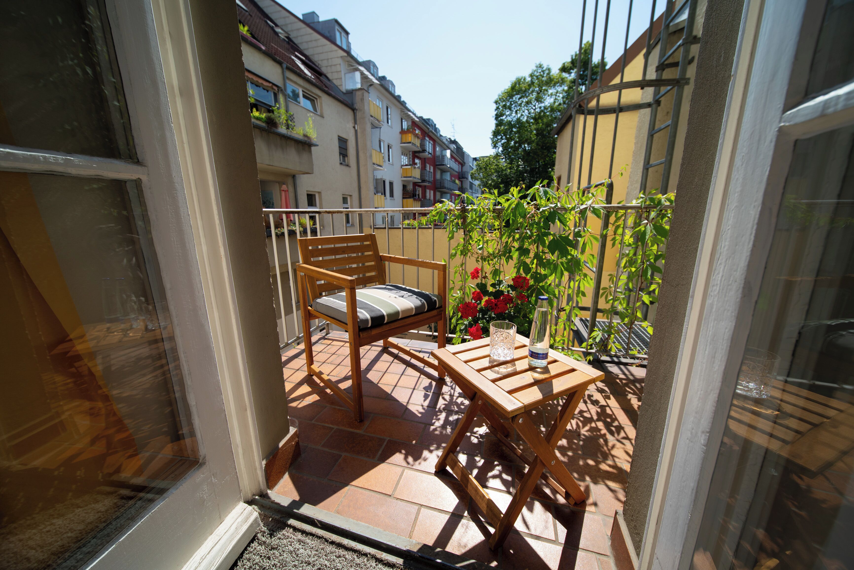 Un balcone con una sedia di legno, un tavolino, una pianta in vaso e un bicchiere di vetro trasparente.