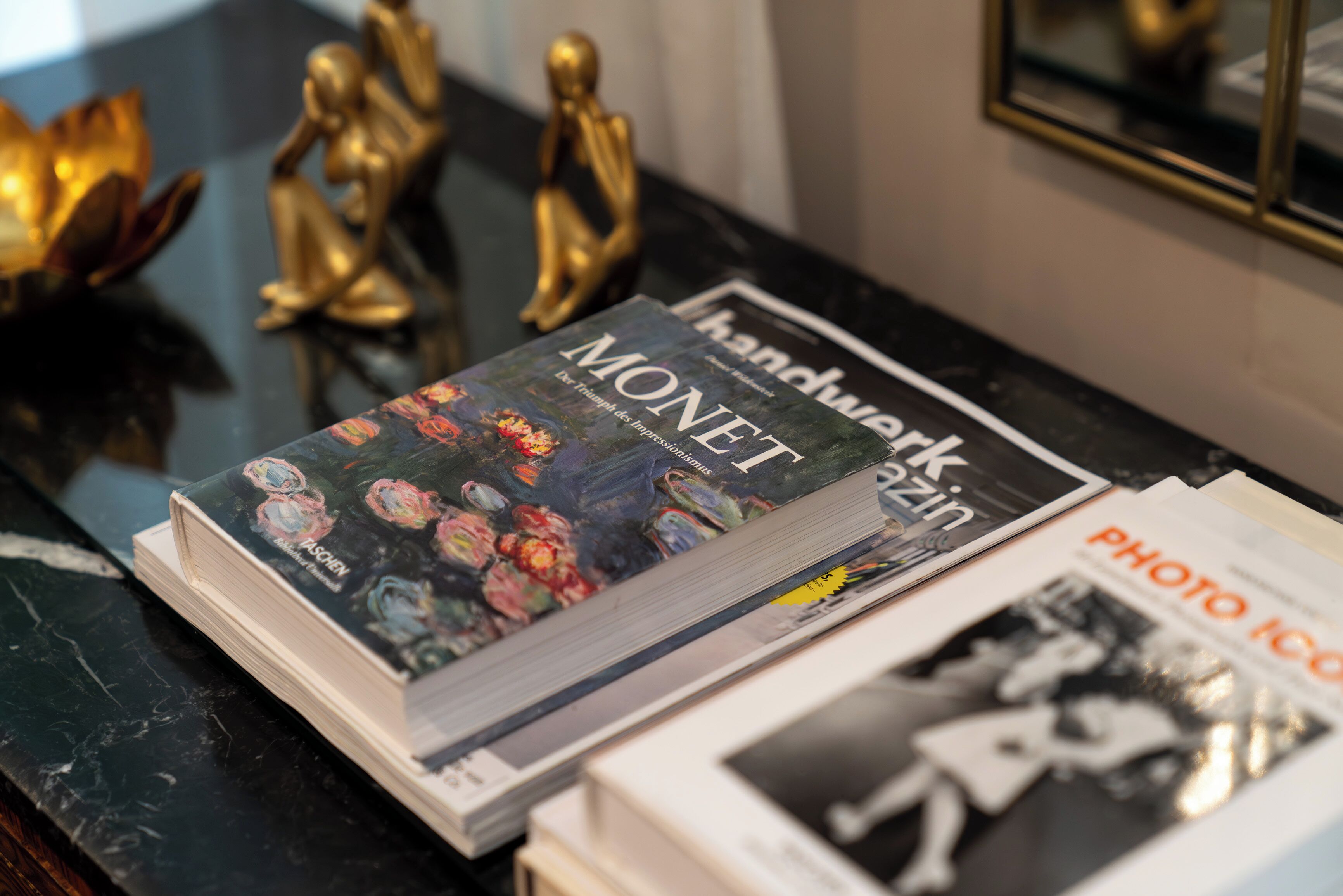 Una revista anomenada 'Handwerk' sobre una superfície de marbre amb figures daurades decoratives i una fotografia emmarcada al fons.