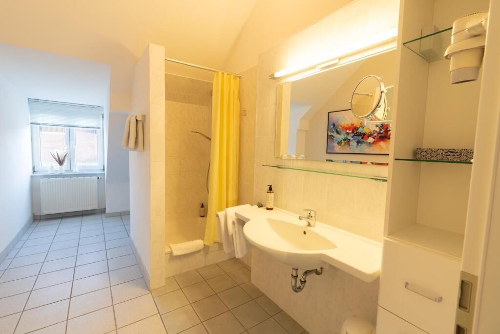Un baño con ducha, lavamanos, espejo y ventana.