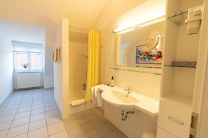 Un bagno con doccia, lavandino, specchio e finestra.