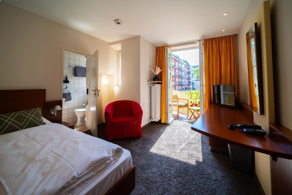 Una camera d'albergo con un letto, una scrivania, una sedia, una televisione e vista sugli edifici.