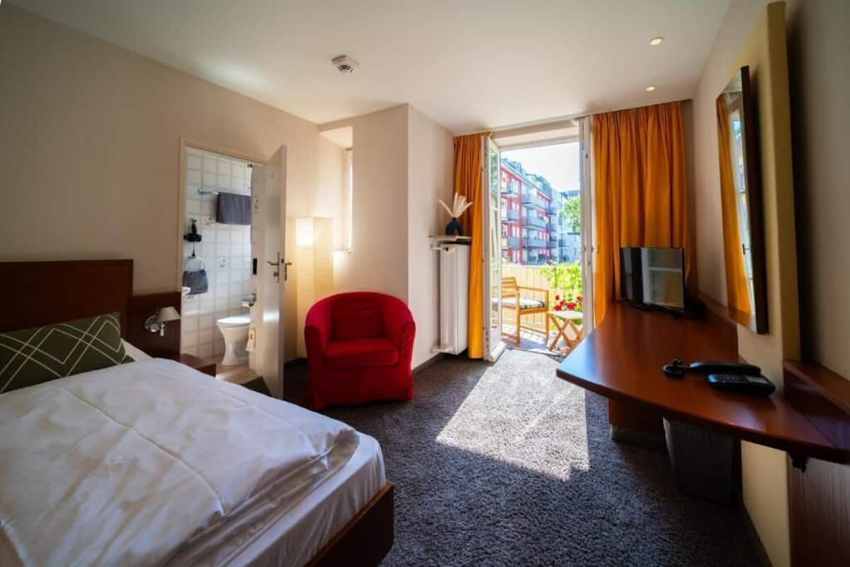 Una camera d'albergo con un letto, una scrivania, una sedia, una televisione e vista sugli edifici.