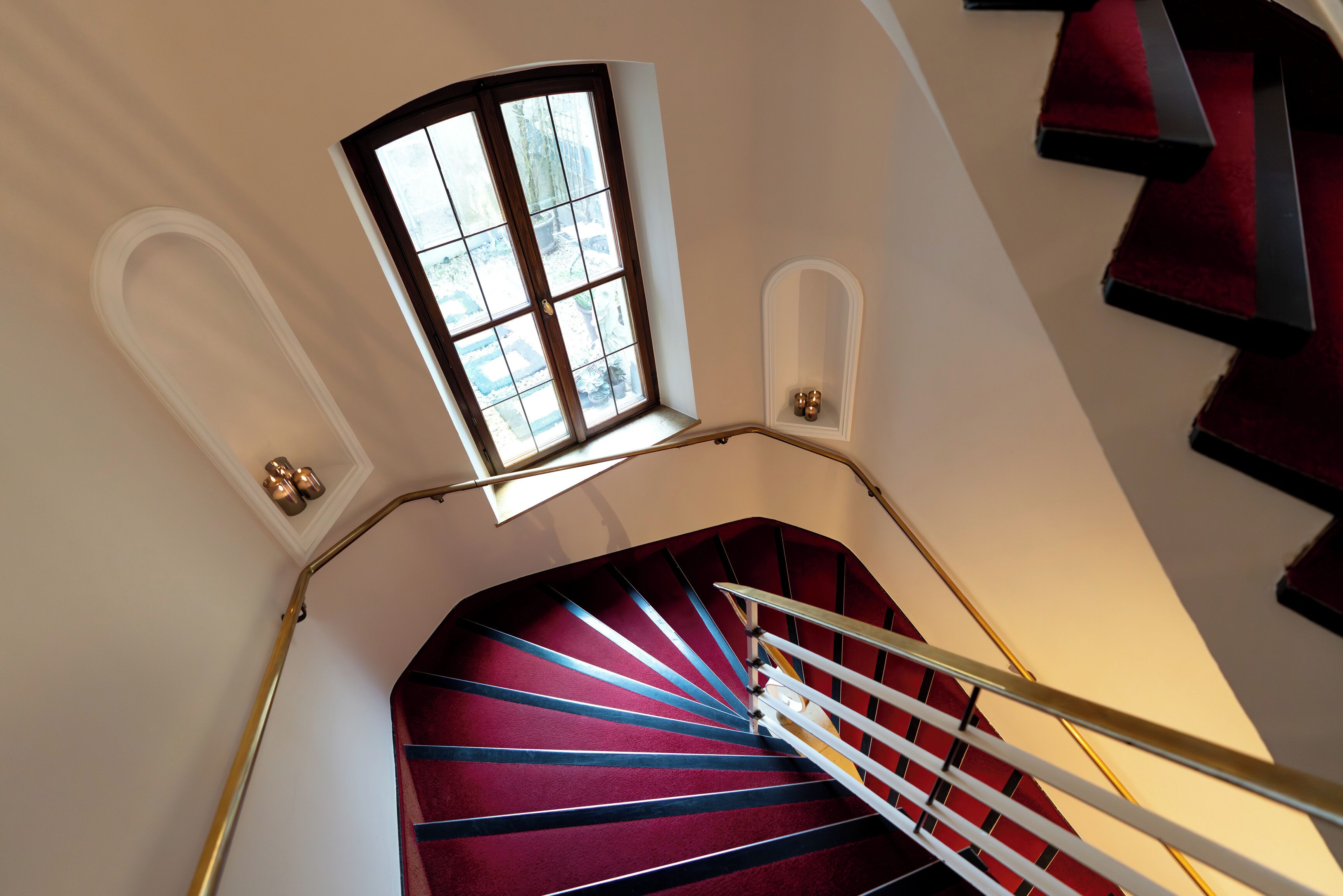 A spiral staircase with a red carpet, a small window at the top, and a handrail.