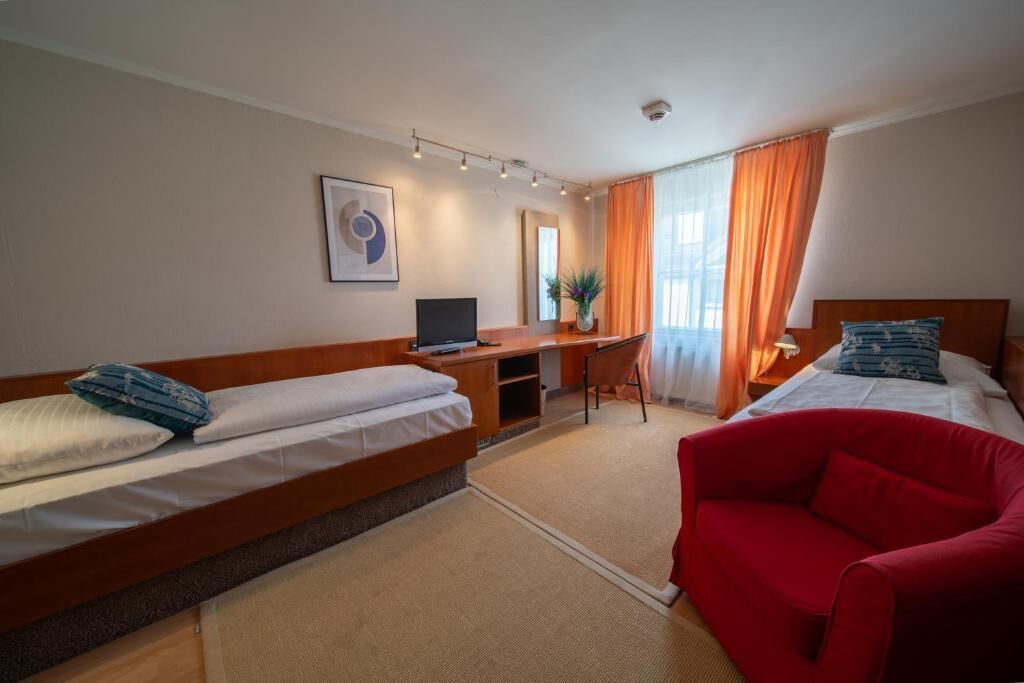 Una camera d'albergo con due letti, una scrivania, una sedia e un divano rosso.