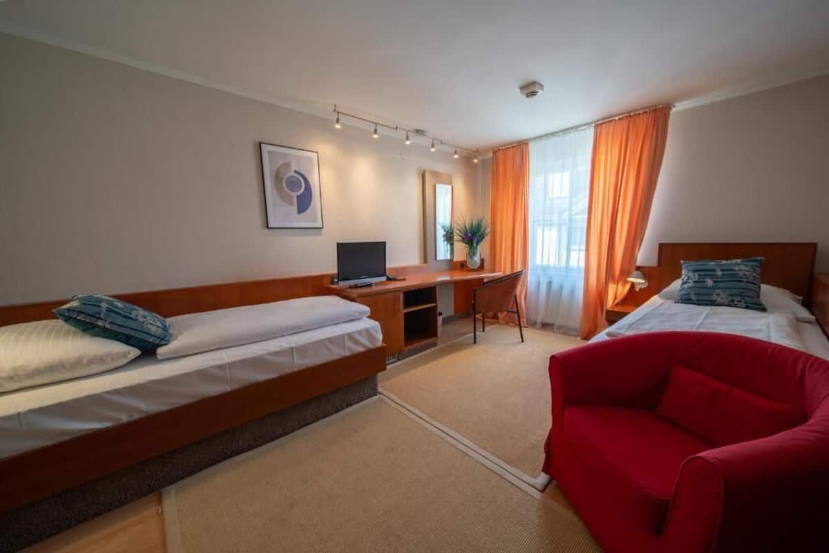 Una camera d'albergo con due letti, una scrivania, una sedia e un divano rosso.