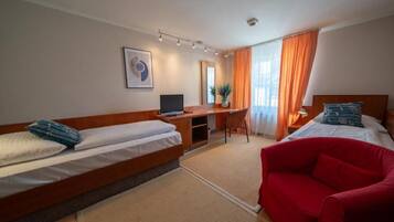 Quarto de hotel com duas camas, uma escrivaninha, uma cadeira e um sofá vermelho.
