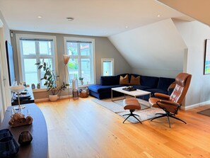 A modern living room with a dark blue sofa, a brown leather chair, and a wooden coffee table. - 3-bedroom apartment in Stavanger city center (Rogaland)