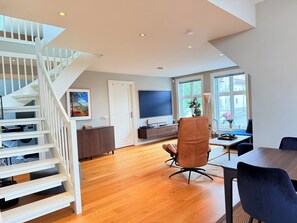 A modern living room with a staircase, a flat-screen TV, and a dining area. - 3-bedroom apartment in Stavanger city center (Rogaland)
