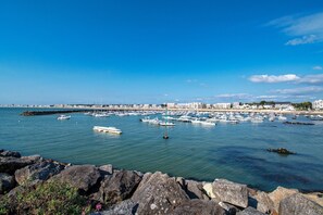 Eine Marina mit zahlreichen vertäuten Booten, einer felsigen Küstenlinie und einer Stadtlandschaft im Hintergrund.