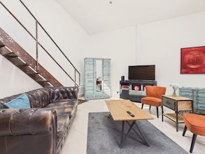 Ein modernes Wohnzimmer mit einer Ledersofa, einem Holztisch, einem Fernseher und einer Treppe.