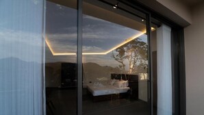 A bedroom with a glass wall, a bed, a nightstand, and a view of the outdoors. - Iris - Kandy (Kandy)