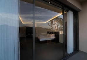 Una camera da letto con parete in vetro, un letto, un comodino e vista sull'esterno.