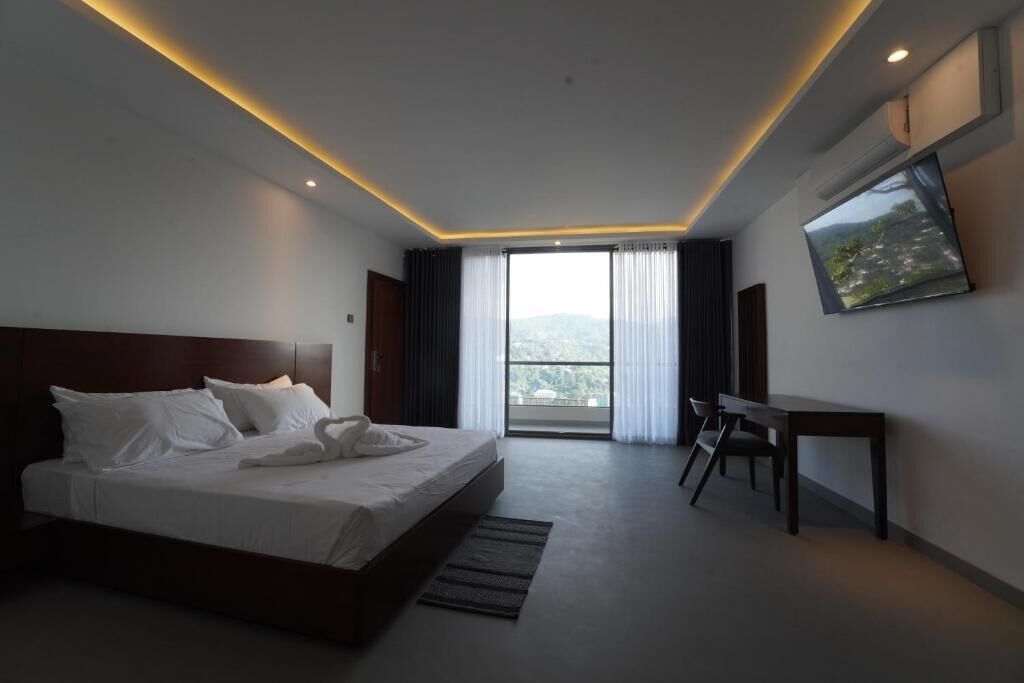 A hotel room with a bed, a desk, a chair, a TV, and a large window with curtains.