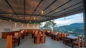 An outdoor dining area with wooden tables and chairs, a bar counter, and a view of a mountainous landscape. - Iris - Kandy (Kandy)