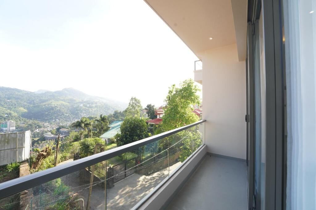Un balcón con barandilla de vidrio que da a un paisaje verde con árboles y edificios.