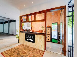 Un espace d’accueil avec un comptoir en bois, un panneau indiquant « Collection » et un réfrigérateur.