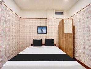 A hotel room with a bed, two black pillows, a wooden wardrobe, a framed picture on the wall, and patterned wallpaper. - Super Collection O Vazhakkala Kakkanad (Kanayannur)