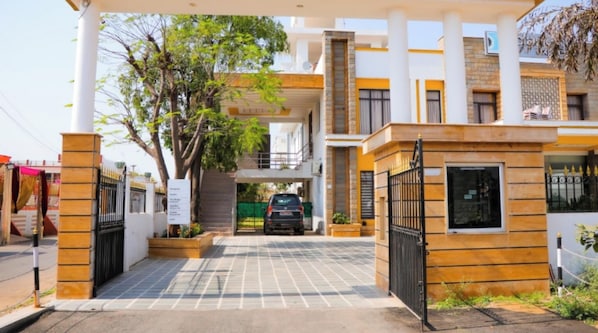 Une entrée sécurisée par un portail, avec une voiture garée à l’intérieur, une allée couverte et un bâtiment à l’architecture moderne.