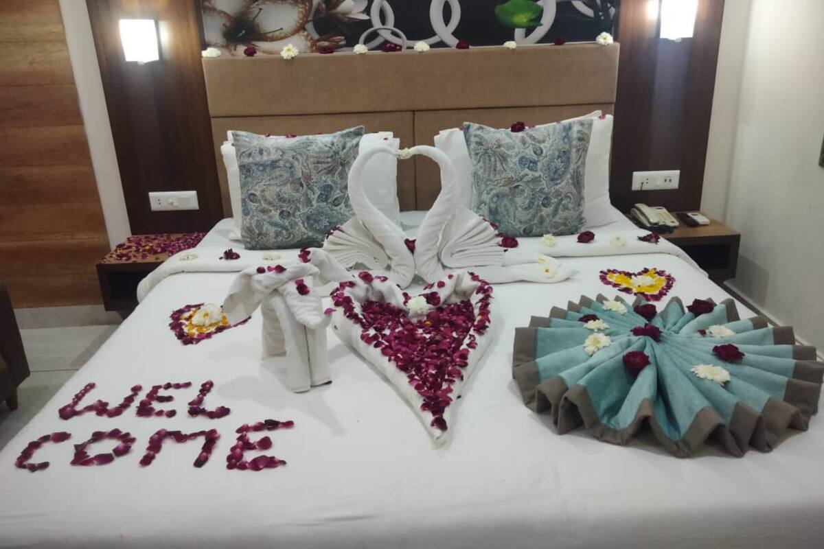 Una cama con un cartel de 'WELCOME' hecho de pétalos de rosa, dos almohadas y un arreglo decorativo con forma de cisne.
