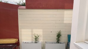 A patio with a patterned tile floor, two blue folding chairs, a yellow cushioned bench, and two white planters with small plants.