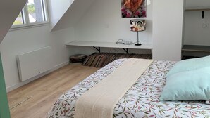 A bedroom with a sloped ceiling, a bed with a patterned bedspread, a decorative wall piece, and a window.