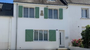 A two-story building with a white facade, green shutters, and a small porch area.