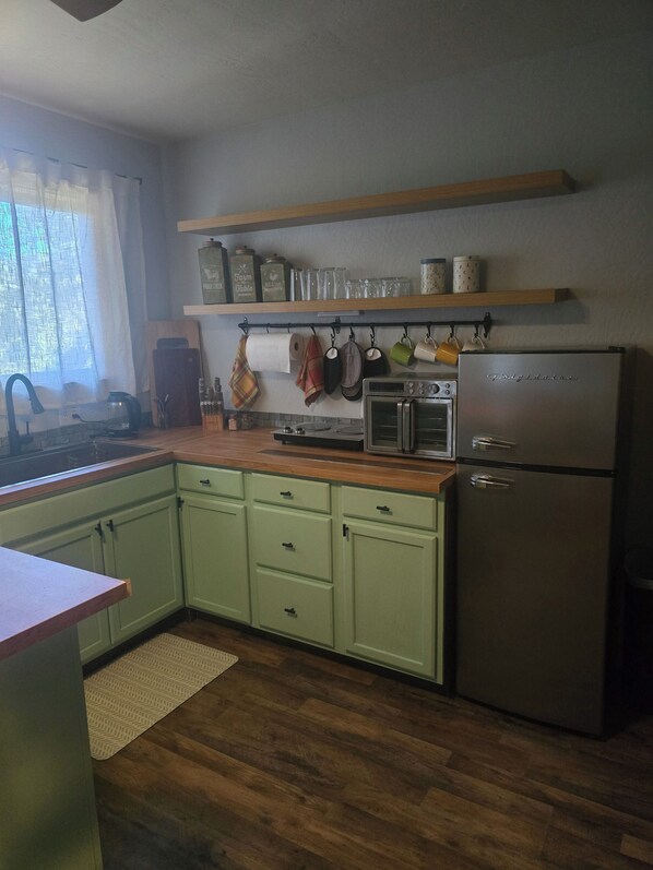 A kitchen with green cabinets, a stainless steel refrigerator, a wooden countertop, and a hanging pot rack.