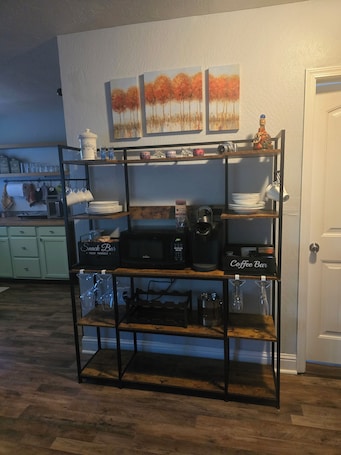 A kitchen with a wooden shelf unit holding kitchenware, a coffee bar, and a microwave.. Walk to downtown Twain Harte from this cozy studio with EV charger.