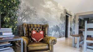 Een leren fauteuil met een rode kussens, een boekenplank met boeken, en een muur met een boommotief.