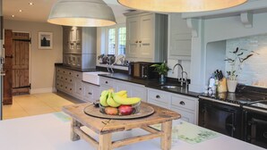 Een keuken met een houten tafel, een schaal fruit en een hanglamp.