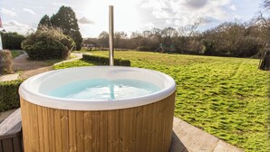 Een hottub in een tuin met een houten terras, omringd door gras en bomen.