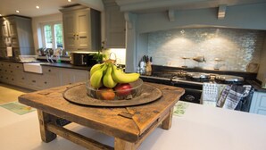 Een keuken met een houten tafel waarop een schaal met fruit, een fornuis en keukenkastjes staan.
