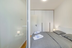 A bedroom with two beds, a wardrobe, and a nightstand with a lamp. - The Oak Haven (Split)